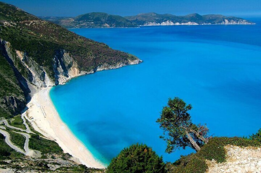 A coastal landscape with a sandy beach, clear blue waters, and a tree in the foreground. 1