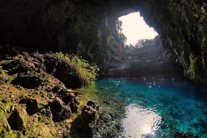A cave entrance with clear blue water and rocky terrain. 3