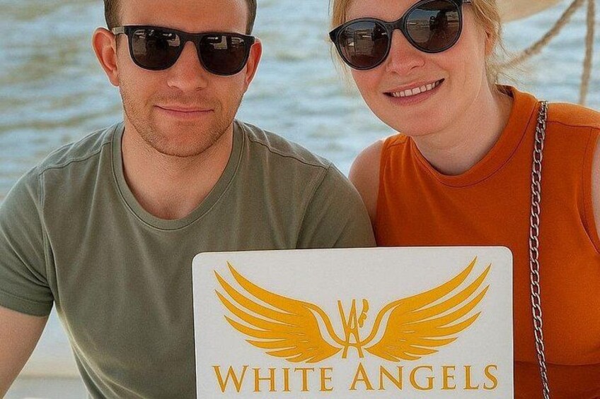 Zwei Personen sitzen in einem Boot, an dem ein Schild mit der Aufschrift 'WHITE ANGELS' befestigt ist. 4