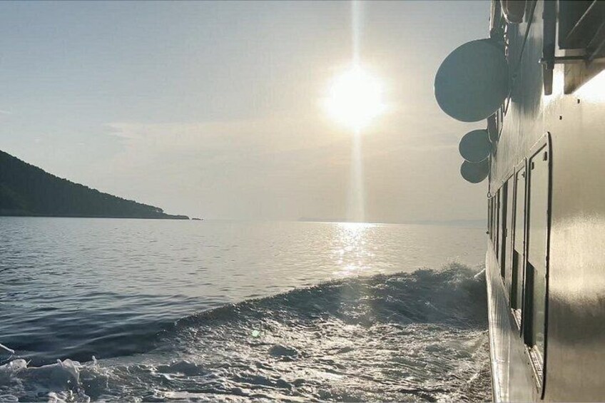 Un bote en un mar tranquilo con el sol bajo en el horizonte, creando un reflejo en el agua. 2