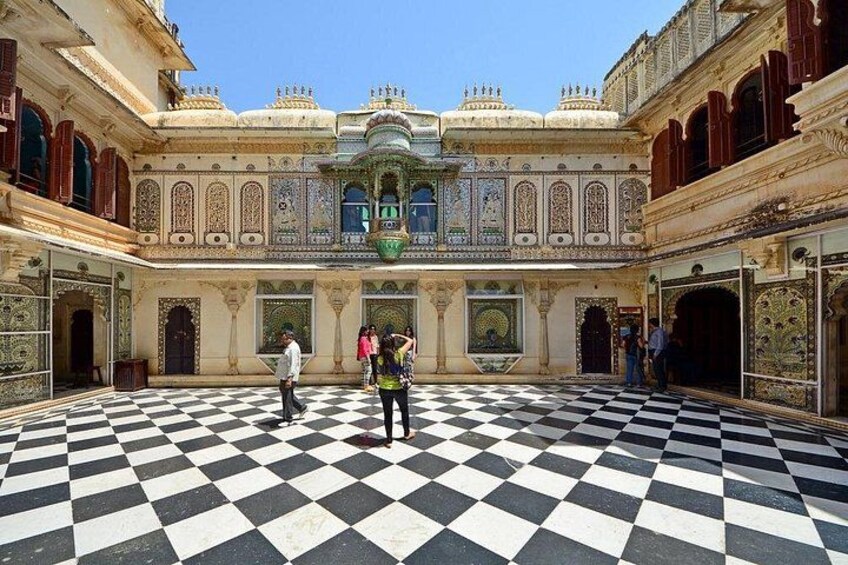 A courtyard with a checkered floor, ornate architecture, and people walking. 3