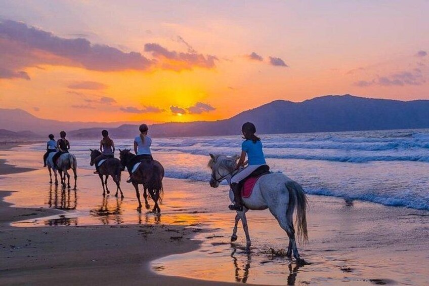 Atardecer sobre una playa con gente montando a caballo. 2