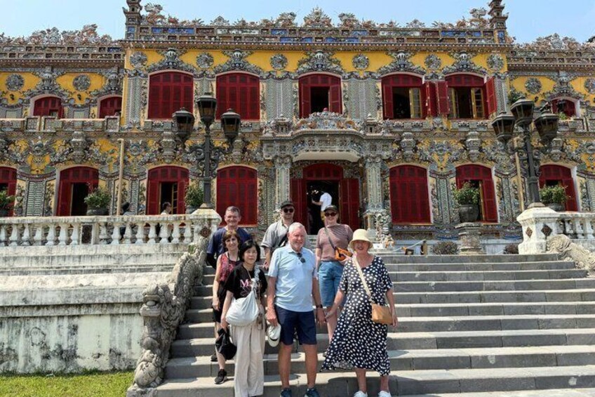A group of people standing in front of a historic building with ornate architecture and red doors. 5