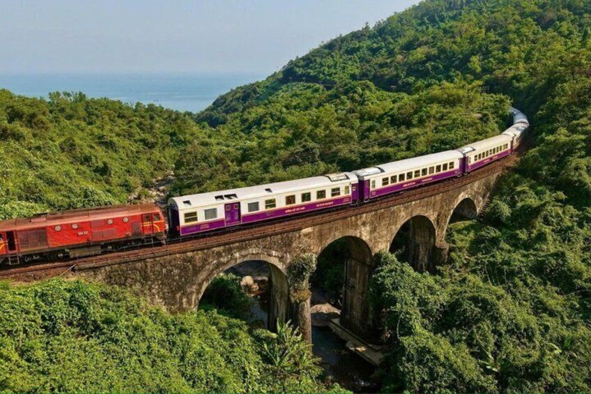 A train crossing a stone bridge over a lush green valley. 1