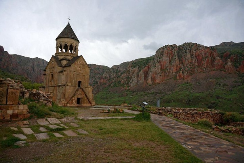 A stone church with a bell tower, surrounded by a grassy area and a stone pathway, set against a mountainous backdrop. 5