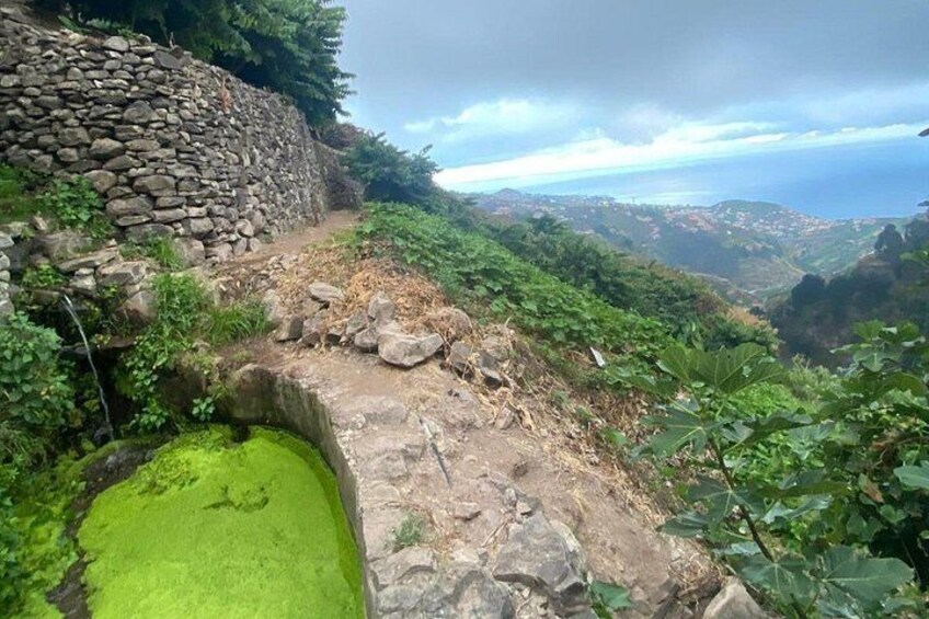 Un muro de piedra, un estanque verde y un paisaje montañoso. 2