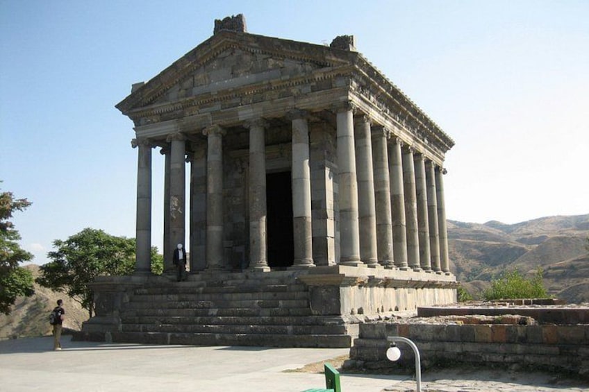 An ancient temple with columns, set against a mountainous backdrop. 1
