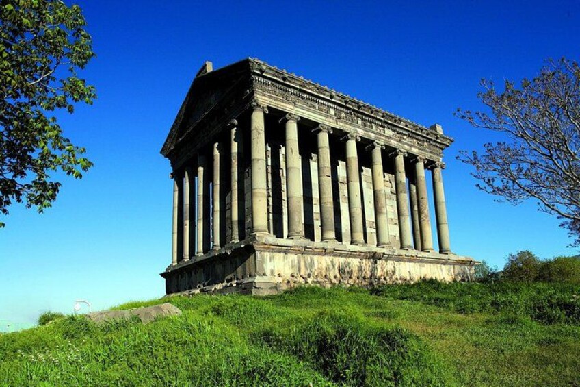 An ancient Greek temple with columns, set on a grassy hill under a clear sky. 2