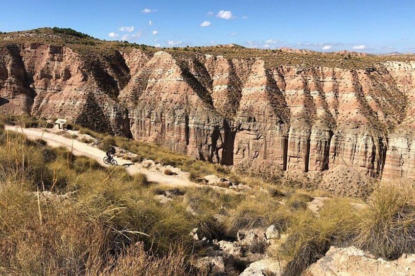 A rugged canyon landscape with a dirt path and a cyclist. 1
