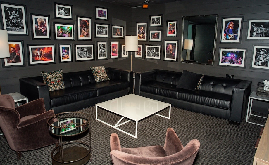 Un salon avec des canapés en cuir noir, une table basse blanche et des affiches encadrées de groupes de rock accrochées au mur. 3