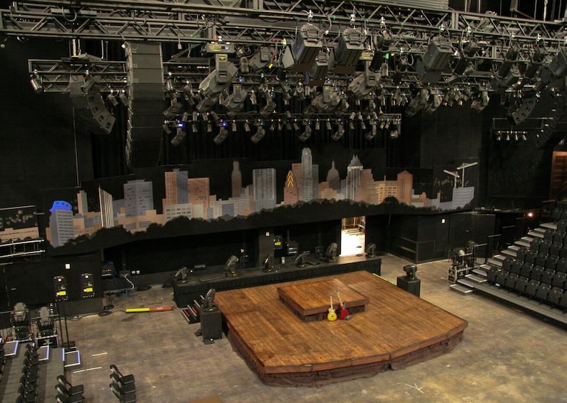 An indoor stage with a wooden platform, lighting equipment, and a cityscape backdrop. 1