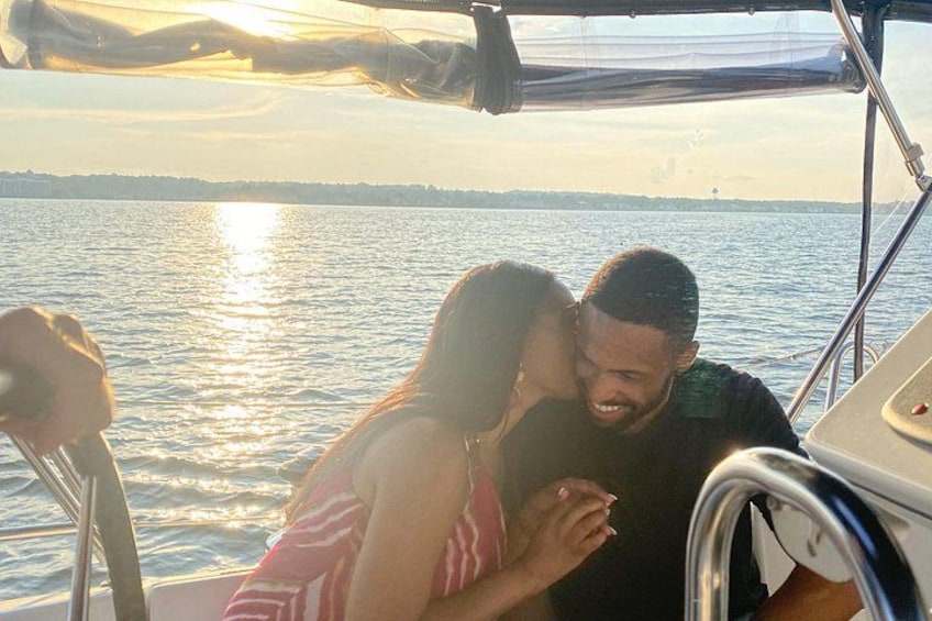 A boat with two people embracing, a body of water, and a distant shoreline. 1