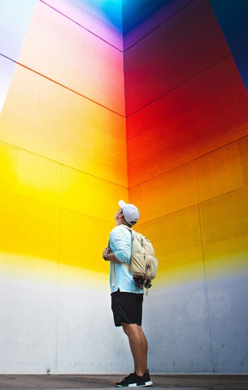 A person standing against a colorful wall with a backpack. 1