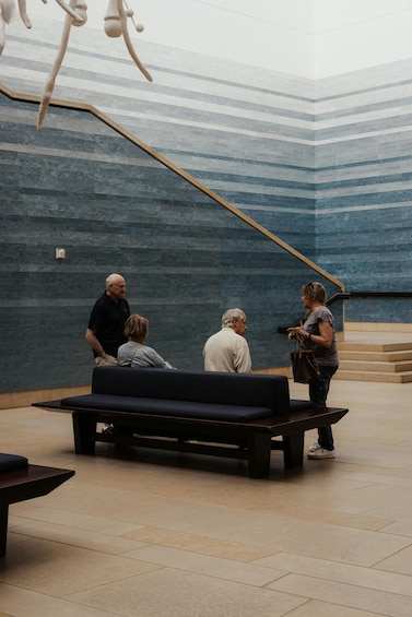 A group of people in a modern interior space with a blue striped wall and a wooden bench. 2