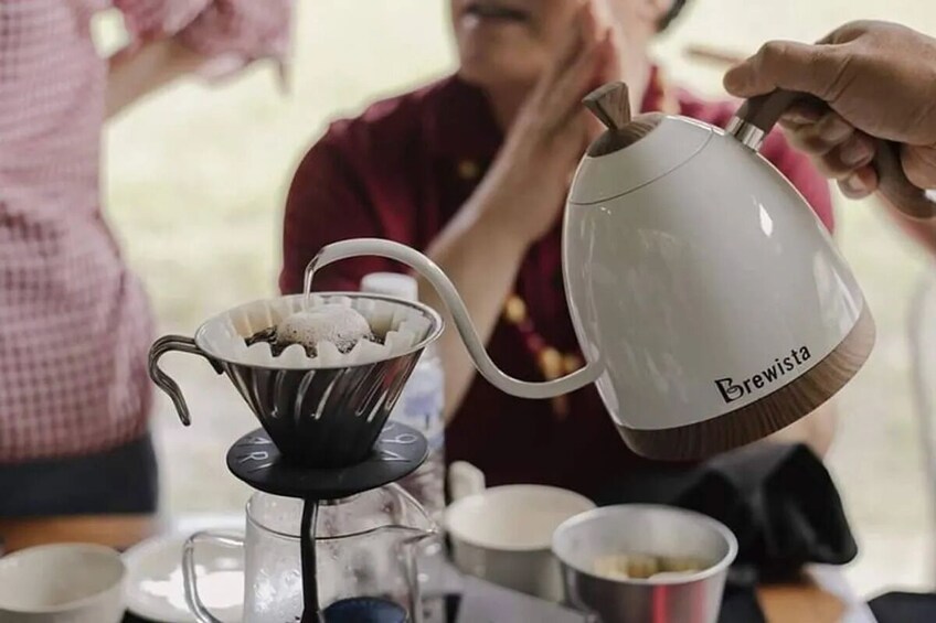 A person pouring coffee from a Brewista kettle into a metal coffee filter. 4