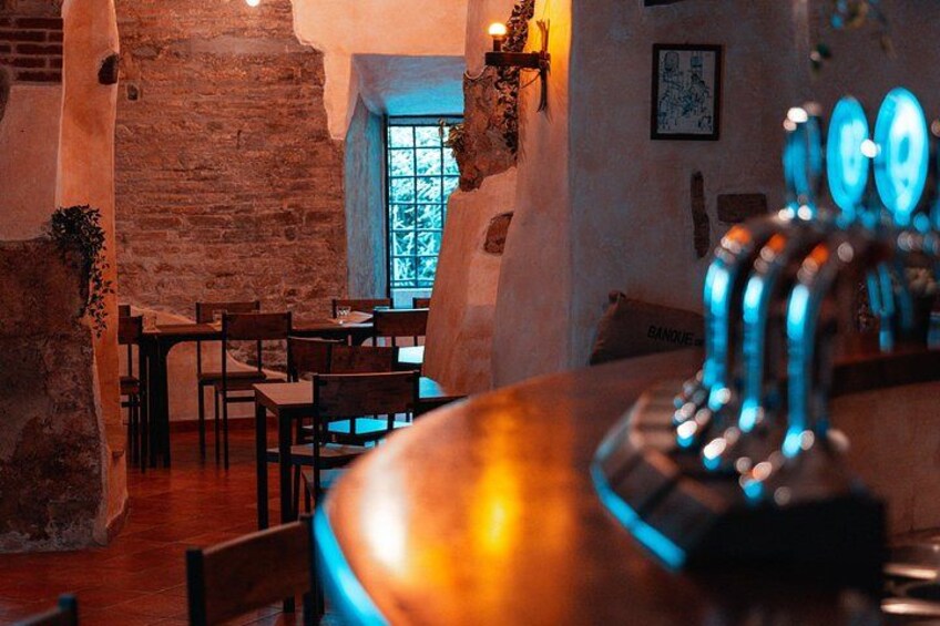 A rustic interior with exposed brick walls, wooden tables, and a bar area with a blue neon light. 5