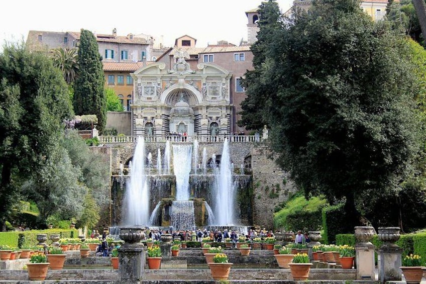 A historic fountain with multiple water jets, surrounded by well-maintained gardens and a classical building in the background. 1