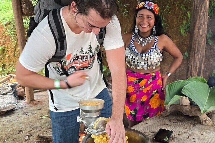 Two people preparing food outdoors, one wearing a white t-shirt and jeans, and the other in a colorful traditional outfit. 1