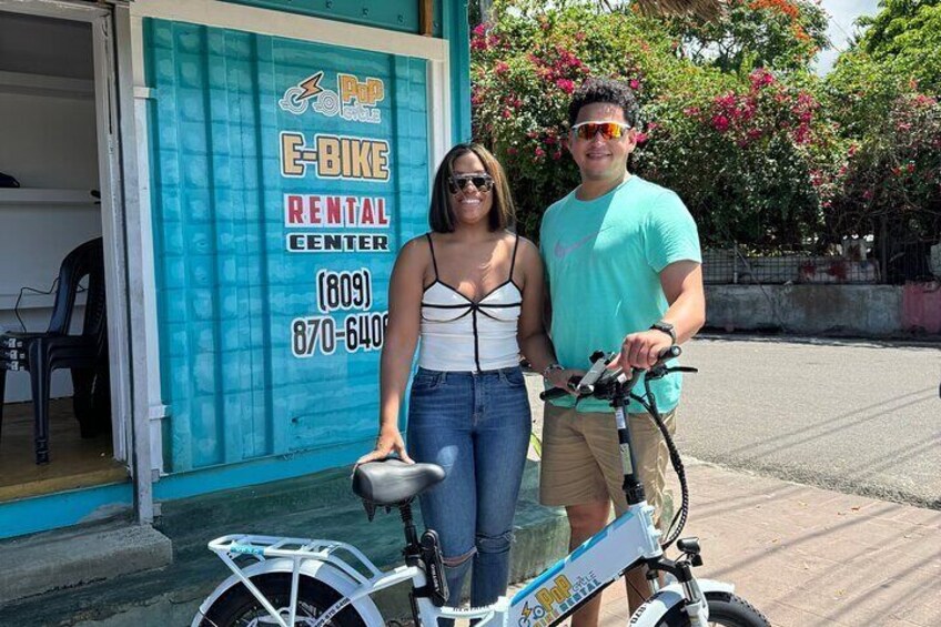 Two people standing in front of a bike rental shop with a bicycle. 2