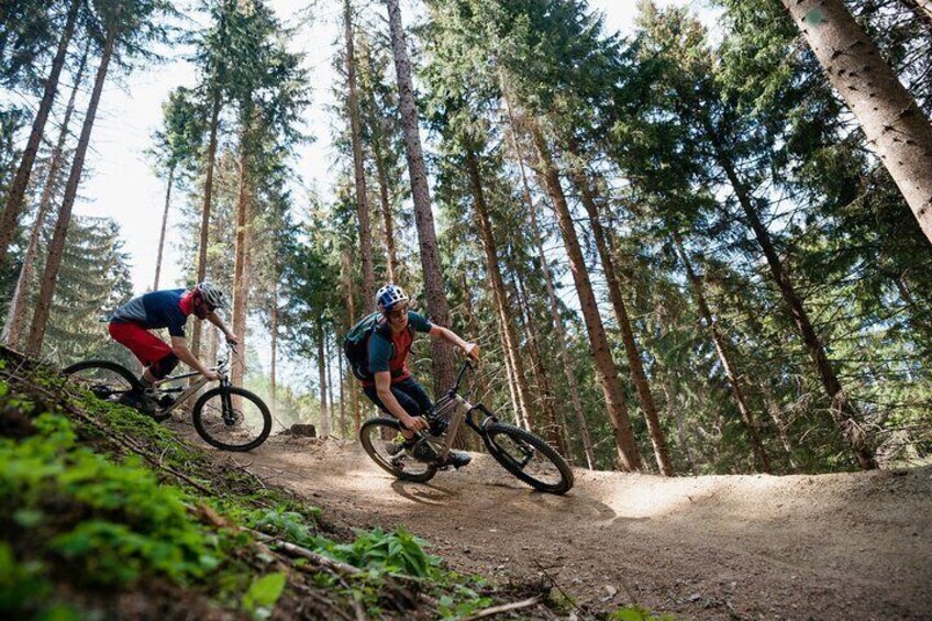 Two mountain bikers on a dirt trail in a forested area. 2
