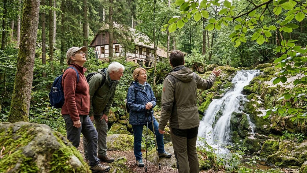 A group of hikers observing a waterfall in a forested area with a traditional house in the background. 3