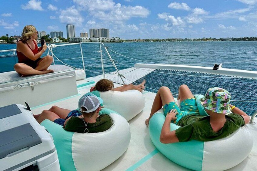 People on a boat, some sitting on inflatable tubes, others on the deck, with a city skyline in the background. 4