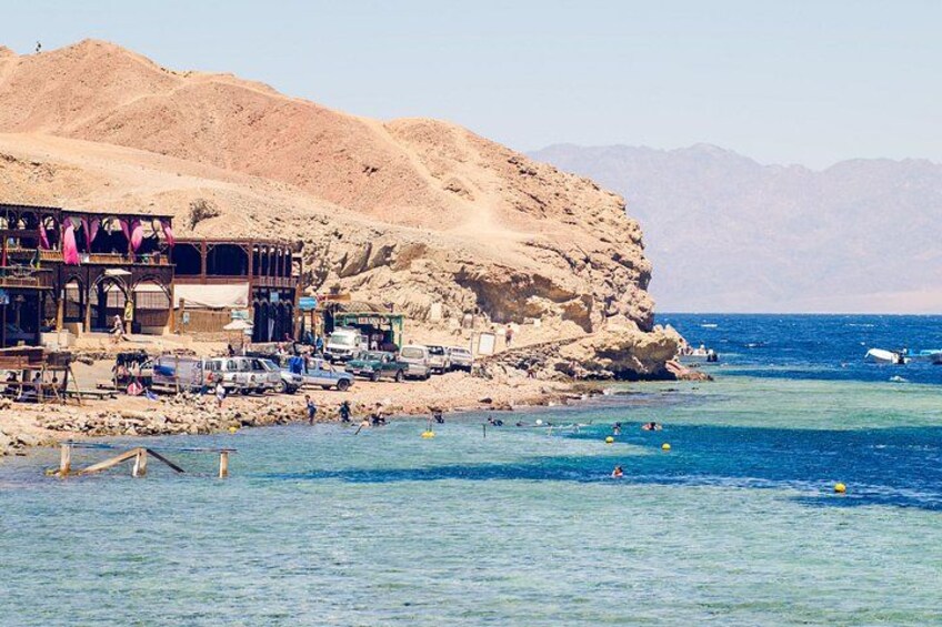A coastal town with a rocky cliff, a pier, and people swimming in the sea. 3
