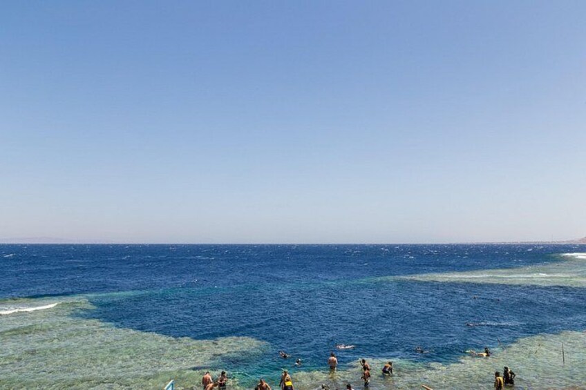 A beach with clear blue water and people swimming. 5