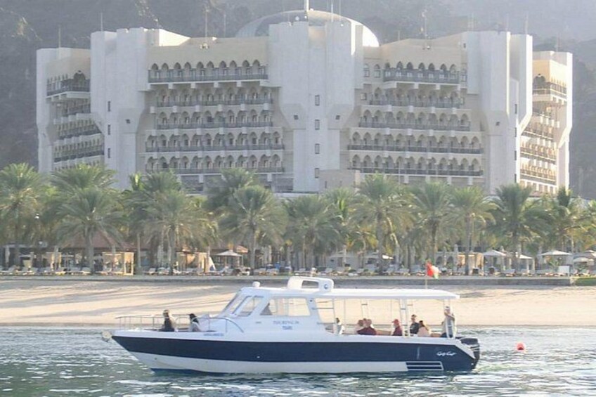 A boat on water with a large building and palm trees in the background. 3