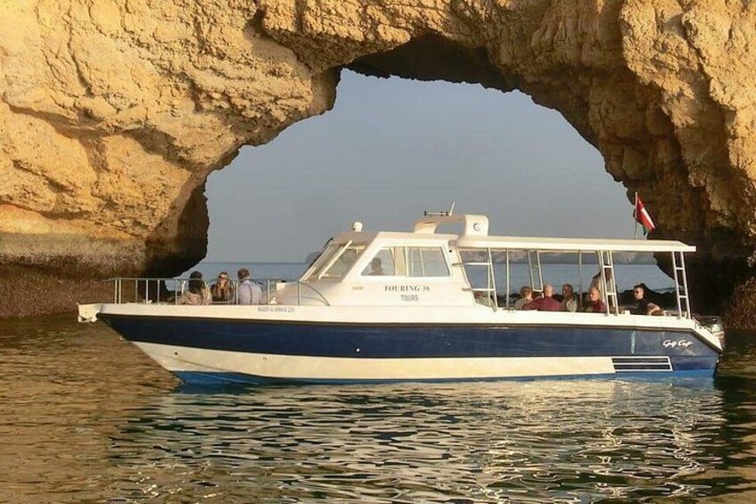 A boat with passengers, a rocky arch formation, and calm water. 2