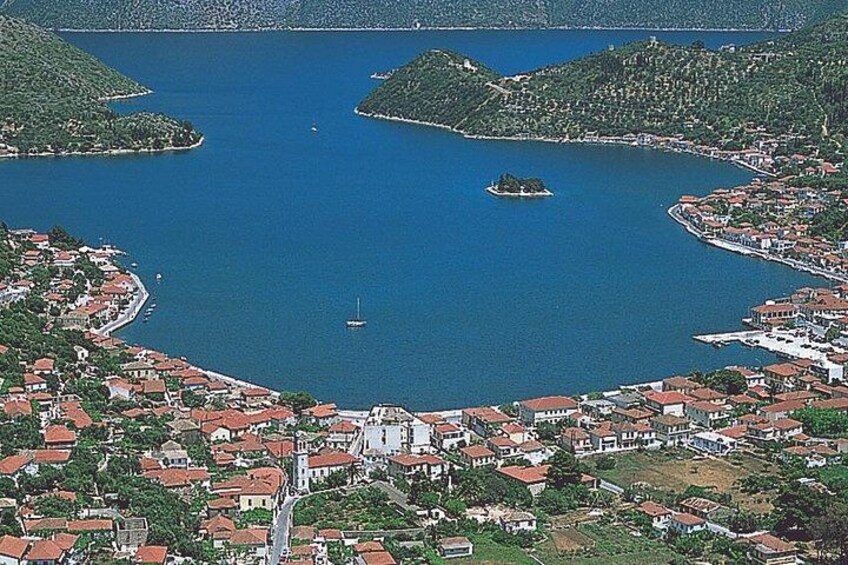 A coastal town with red-roofed buildings, a small island, and a clear blue sea. 2