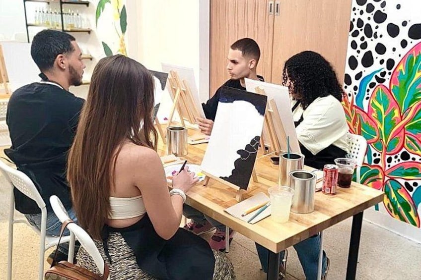 A group of people engaged in painting, with art supplies and canvases on a table. 5