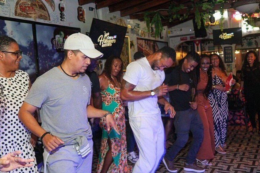 A group of people dancing in a room with a patterned floor and posters on the wall. 5