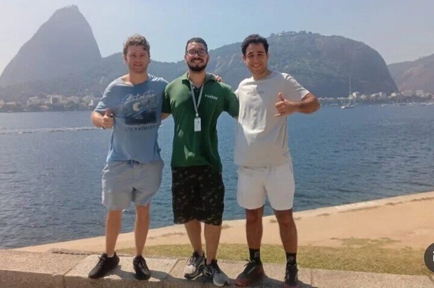 Three people standing by a waterfront with a mountain in the background. 2
