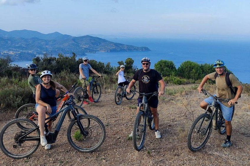 A group of cyclists on a dirt path with a scenic view of the ocean and hills in the background. 2