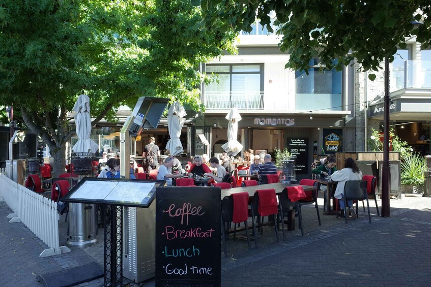 An outdoor café with tables and chairs, a menu board, and a signboard listing coffee, breakfast, lunch, and good time. 2