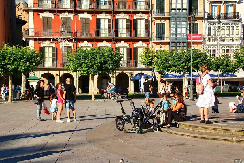 A bustling public square with people walking, sitting, and children playing. 1