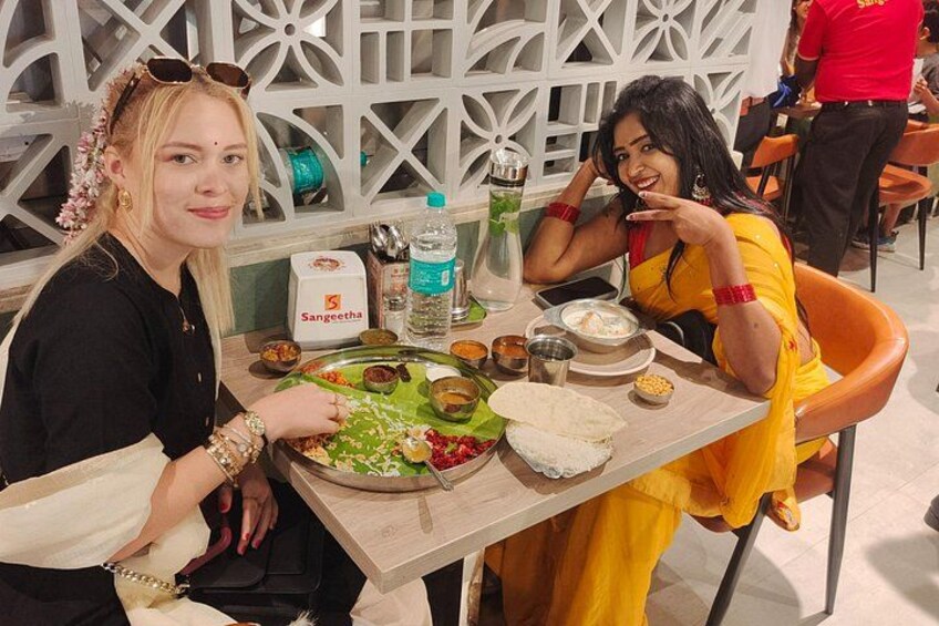 Two people sitting at a table with a meal, a bottle of water, and a Sangeetha brand bottle. 1