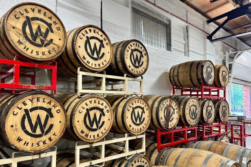 Barili di legno impilati su scaffali, con l'etichetta 'Cleveland Whiskey' ben visibile. 1