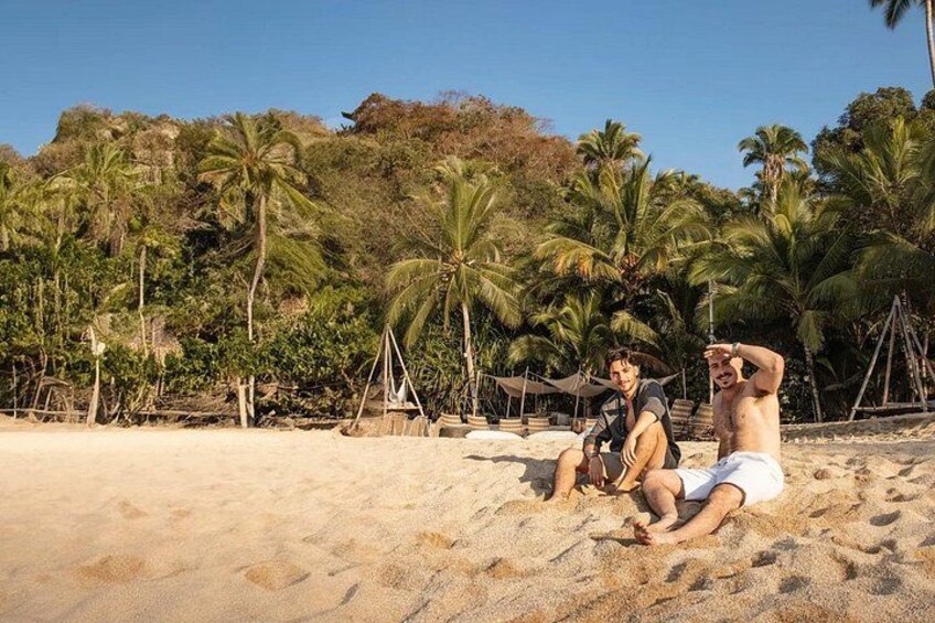 Due persone sedute su una spiaggia sabbiosa con palme e un cielo sereno sullo sfondo. 4