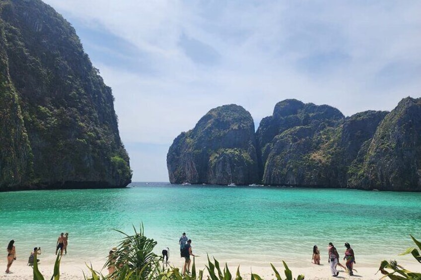 Une plage à l’eau turquoise et limpide, des gens se promenant le long du rivage, et de grandes falaises calcaires en arrière-plan. 5