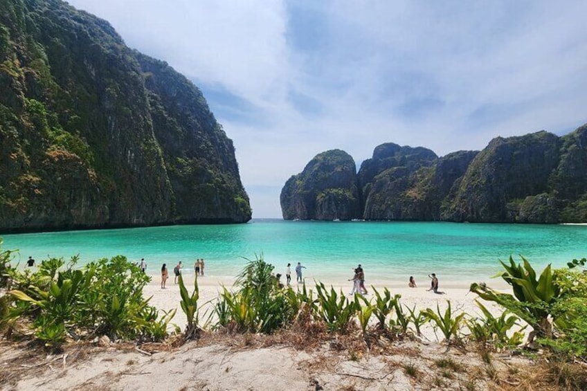 Une plage à l’eau turquoise et limpide, des gens qui se prélassent au soleil et de luxuriantes falaises verdoyantes. 3