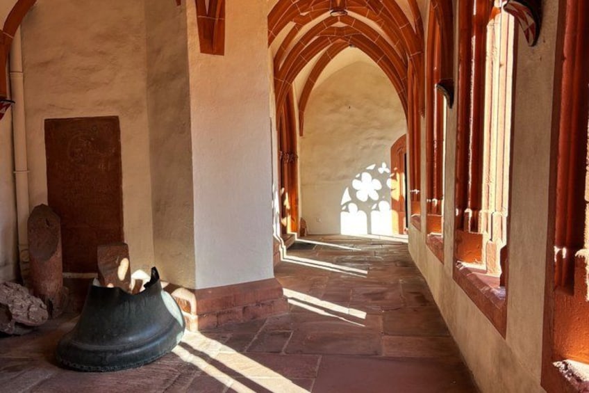 A stone corridor with arches, a large stone basin, and sunlight filtering through windows. 1
