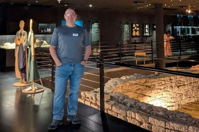 A man standing in a museum with exhibits including a stone wall and a mannequin. 2
