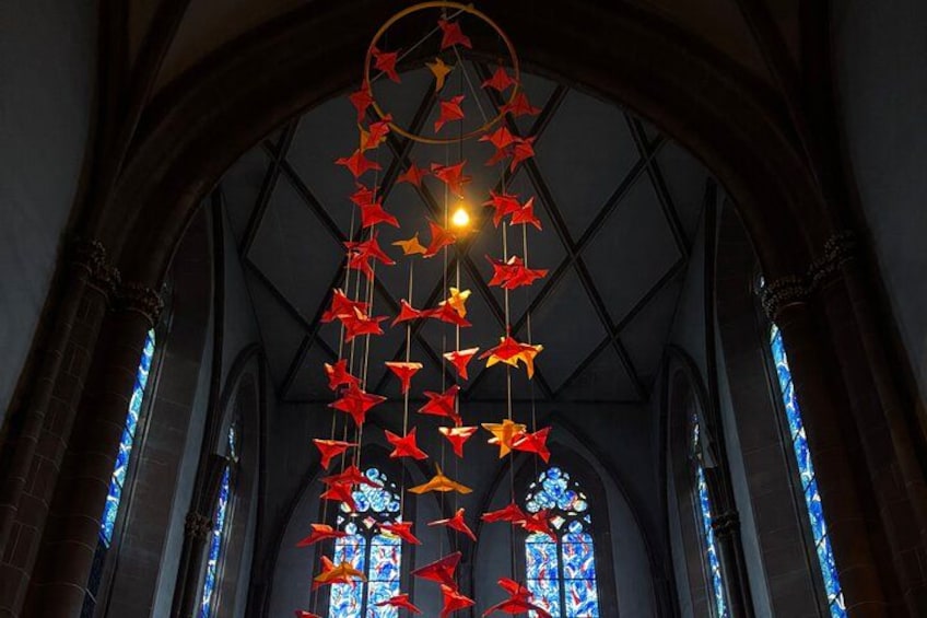 A church interior with stained glass windows and a hanging decoration of red and orange paper stars. 3