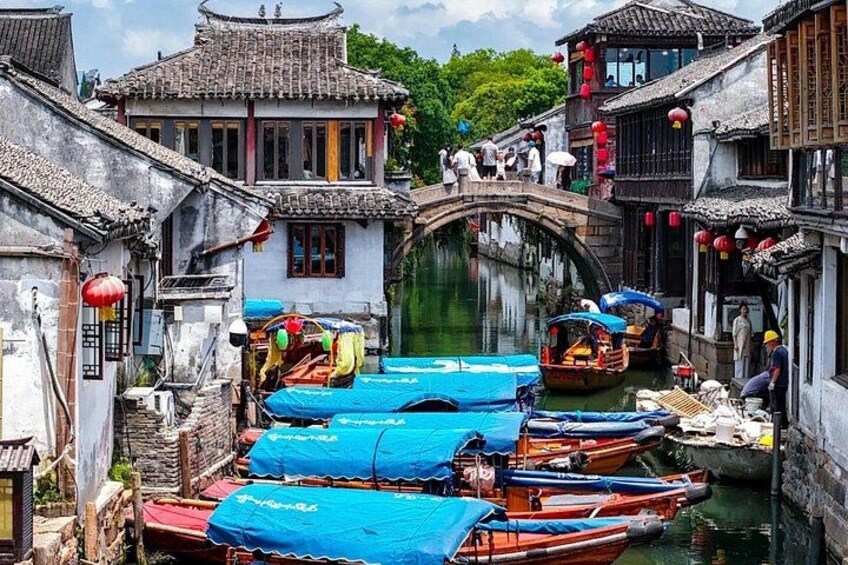A traditional Chinese water town with narrow canals, wooden boats, and tiled-roofed buildings. 1