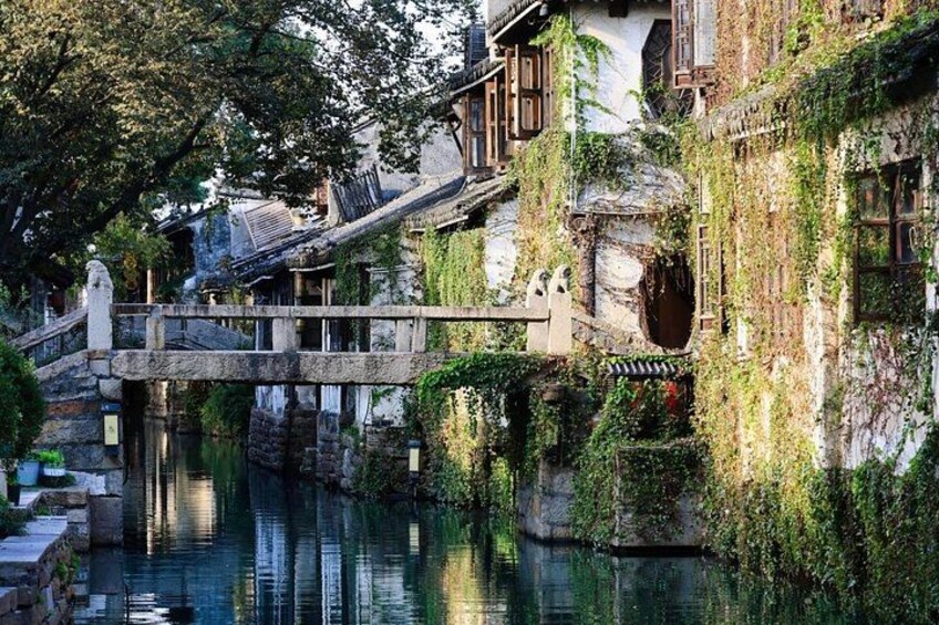 A traditional Chinese water town with a stone bridge over a canal, surrounded by lush greenery and historic buildings. 5
