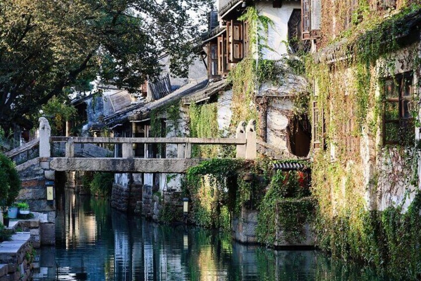 Een traditionele Chinese brug over een rustige rivier, omringd door weelderige begroeiing en historische gebouwen. 5