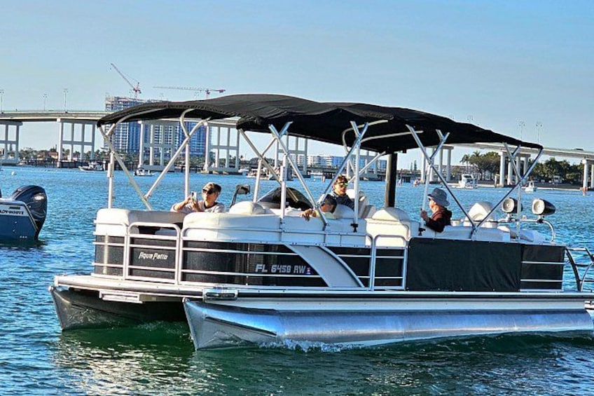 A pontoon boat with a canopy, docked near a bridge. 3