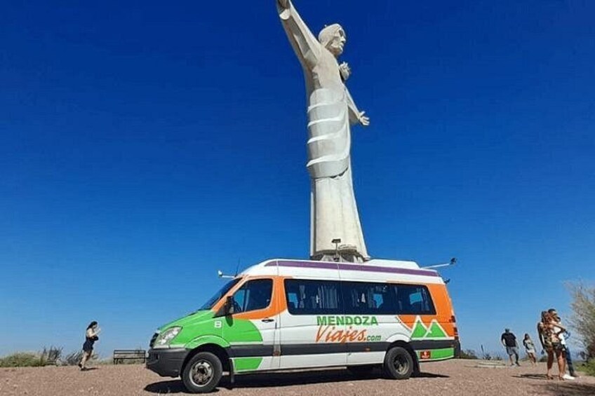 Ein Van mit der Aufschrift 'Mendoza Viagens.com' parkt vor einer großen Statue. 4